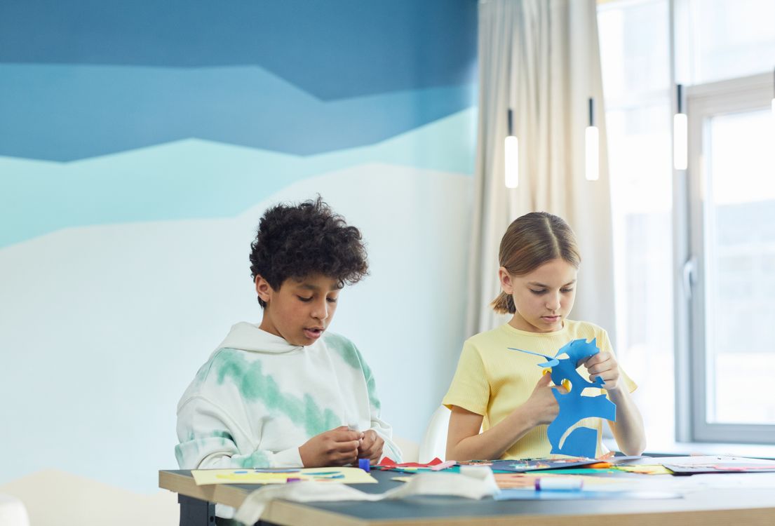 Zwei Kinder basteln am Tisch mit buntem Papier und Schere