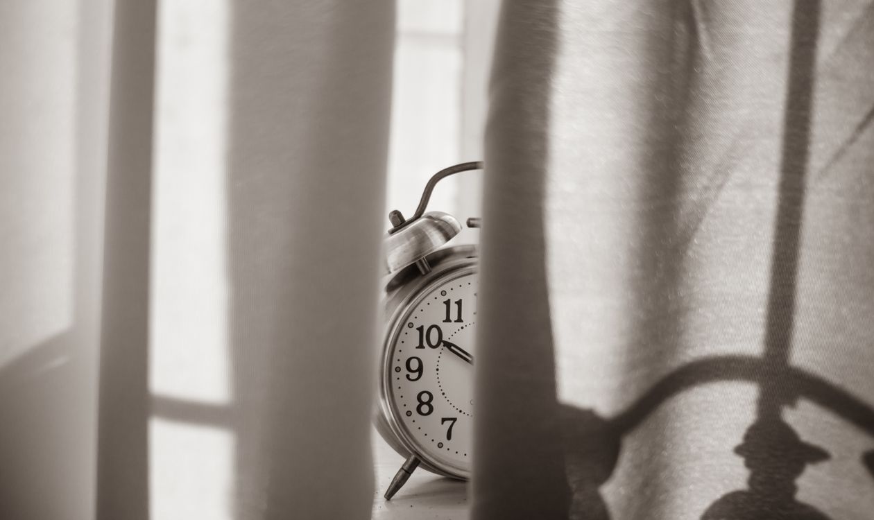 Ein Wecker auf der Fensterbank, halb hinter dem Vorhang